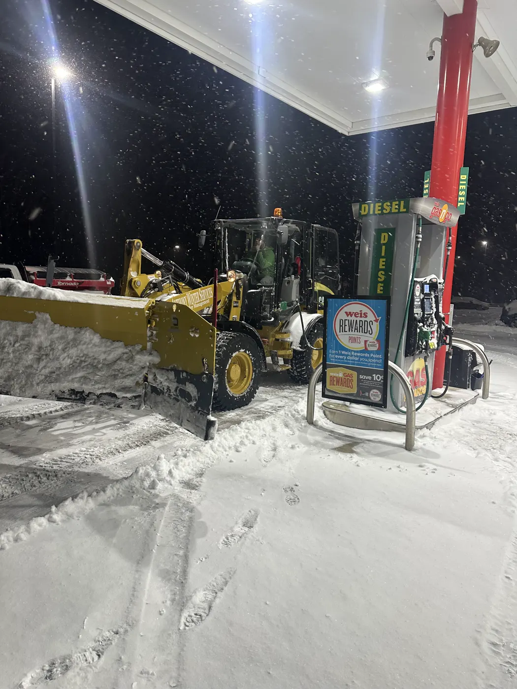 Loader with a containment pusher clearing a gas station apron during a snowfall
