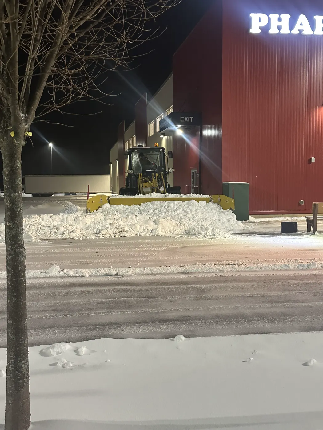 Loader clearing snow beside a lit storefront at night