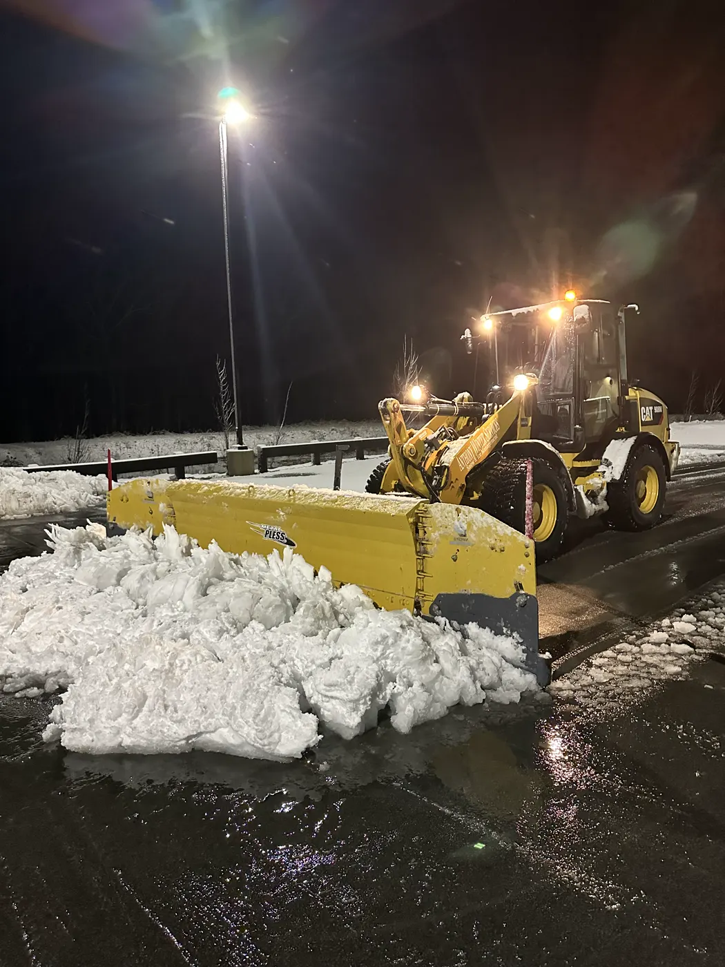 Loader pushing a large pile of snow across a lit commercial lot at night
