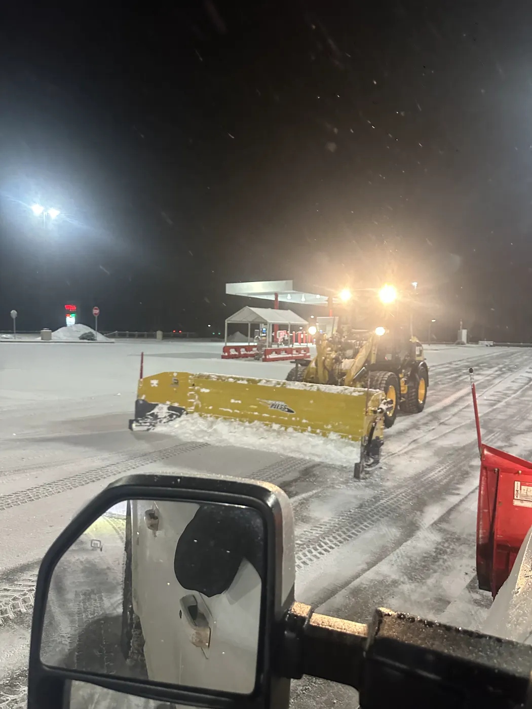 Loader with a yellow containment pusher clearing a commercial parking lot at night