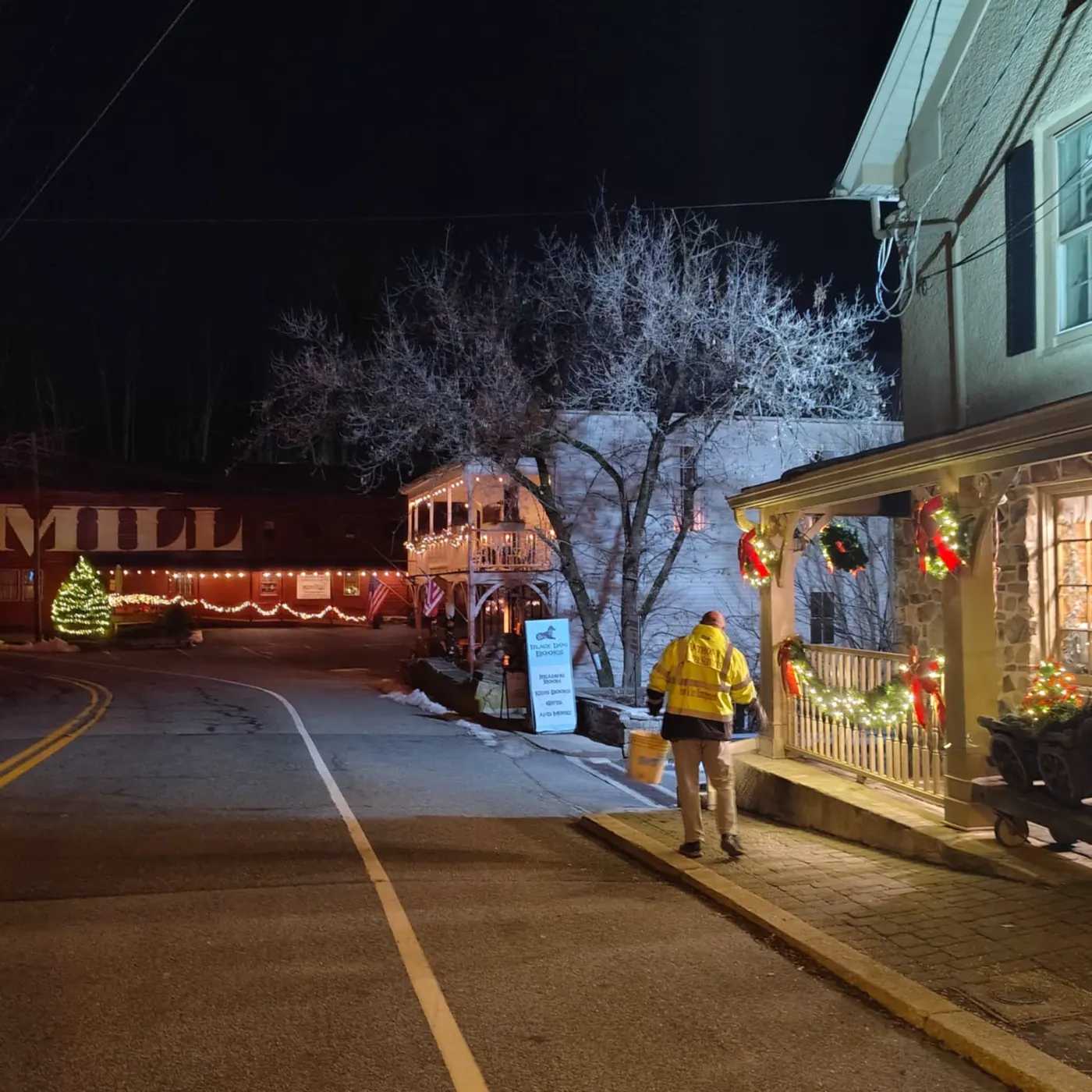 Crew member in a high-visibility jacket clearing a storefront sidewalk at night